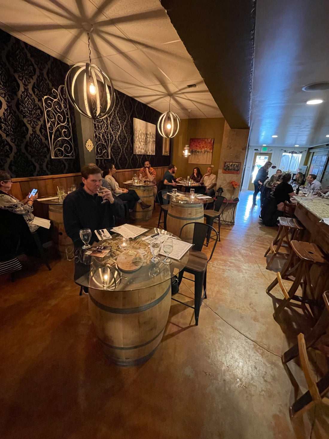 A small restaurant with every table occupied. There is a man sipping a whiskey at one of the tables.
