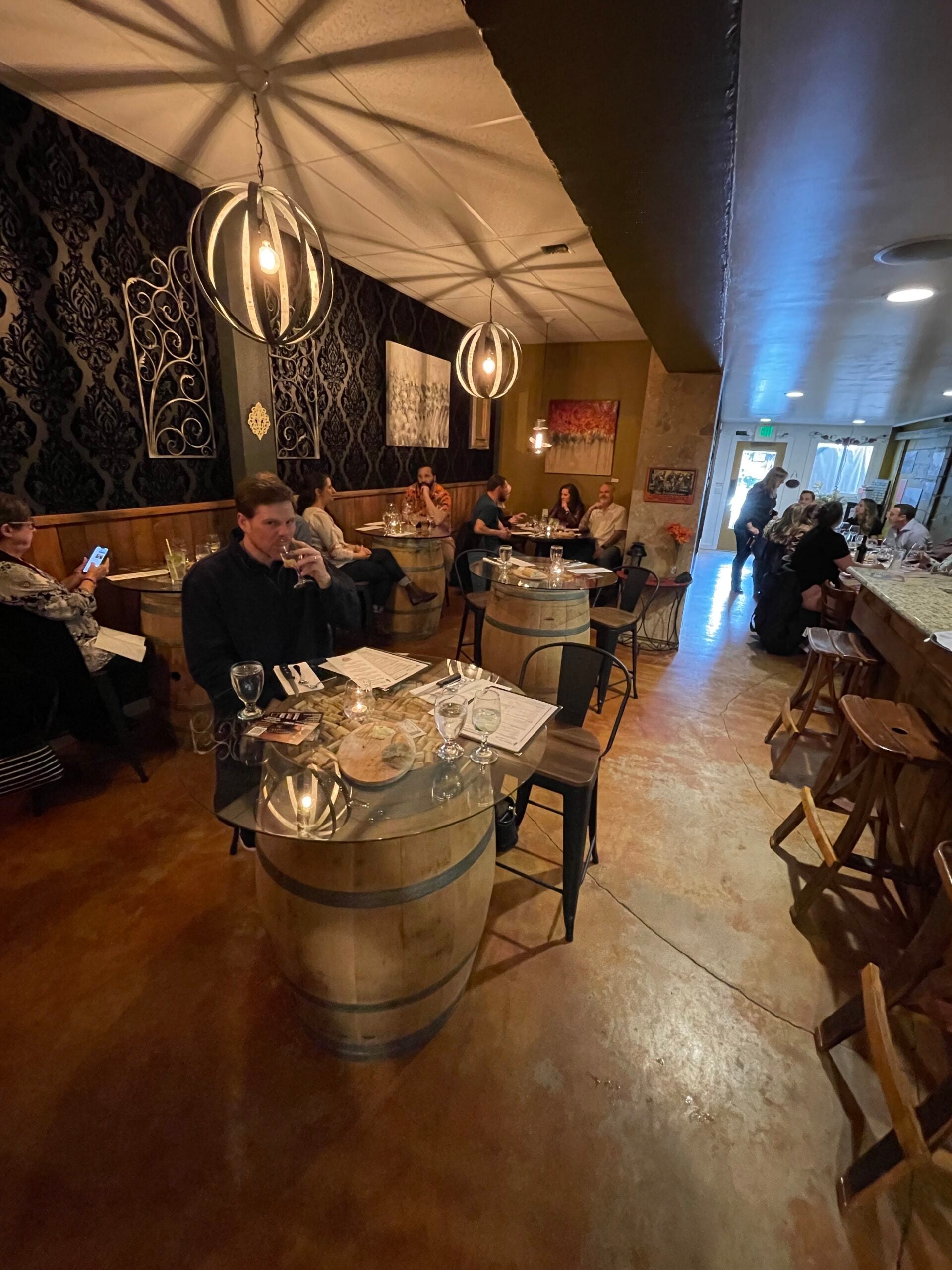 A small restaurant with every table occupied. There is a man sipping a whiskey at one of the tables.
