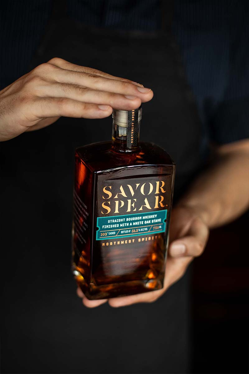 A man is holding a bottle of Savor Spear® Straight Bourbon Whiskey in his hands