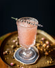 Pink cocktail in a glass with lavender garnish on a dark background