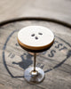 Bourbon cocktail with a creamy top layer on a wooden barrel background