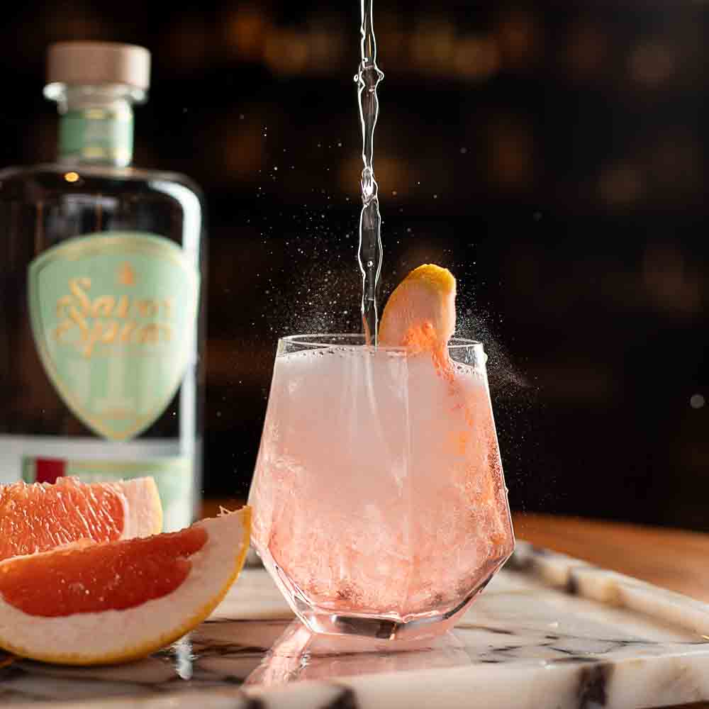 Cocktail being poured into a glass with a bottle of St. Spitz in the background