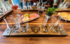 Wooden tray with glasses of alcohol and a plate of food on a wooden table.