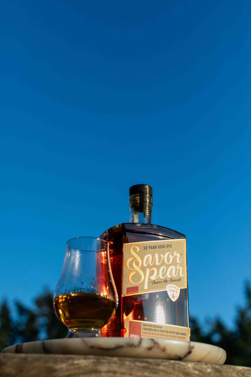 Bottle of Savor Spear whiskey with a glass of whiskey against a blue sky background