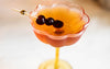 Cocktail in a decorative glass with cherries on a stick against a neutral background