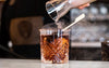Bartender pouring a cocktail into a glass with a smoking shaker, blurred bar background