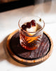 Glass of amber liquid with cherries on a wooden coaster