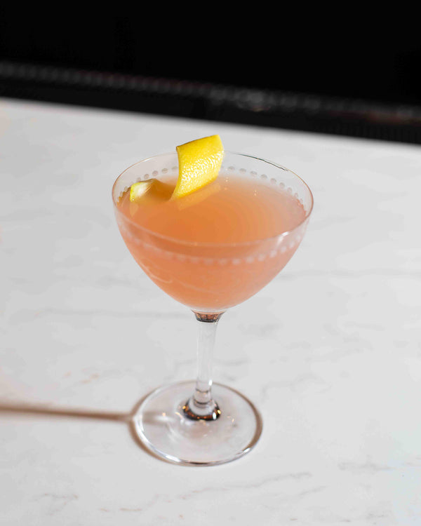 Blush pink cocktail in a dotted coupe glass with a lemon twist garnish, served on a white marble bar at Northwest Spirits