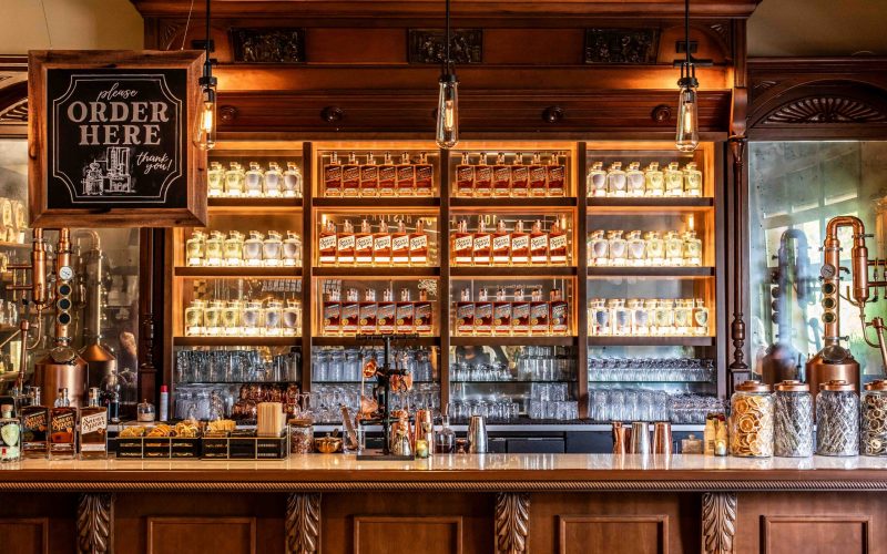 Bar with wooden shelves stocked with bottles and a 'Please Order Here' sign.