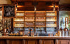 Bar with wooden shelves stocked with bottles and a 'Please Order Here' sign.