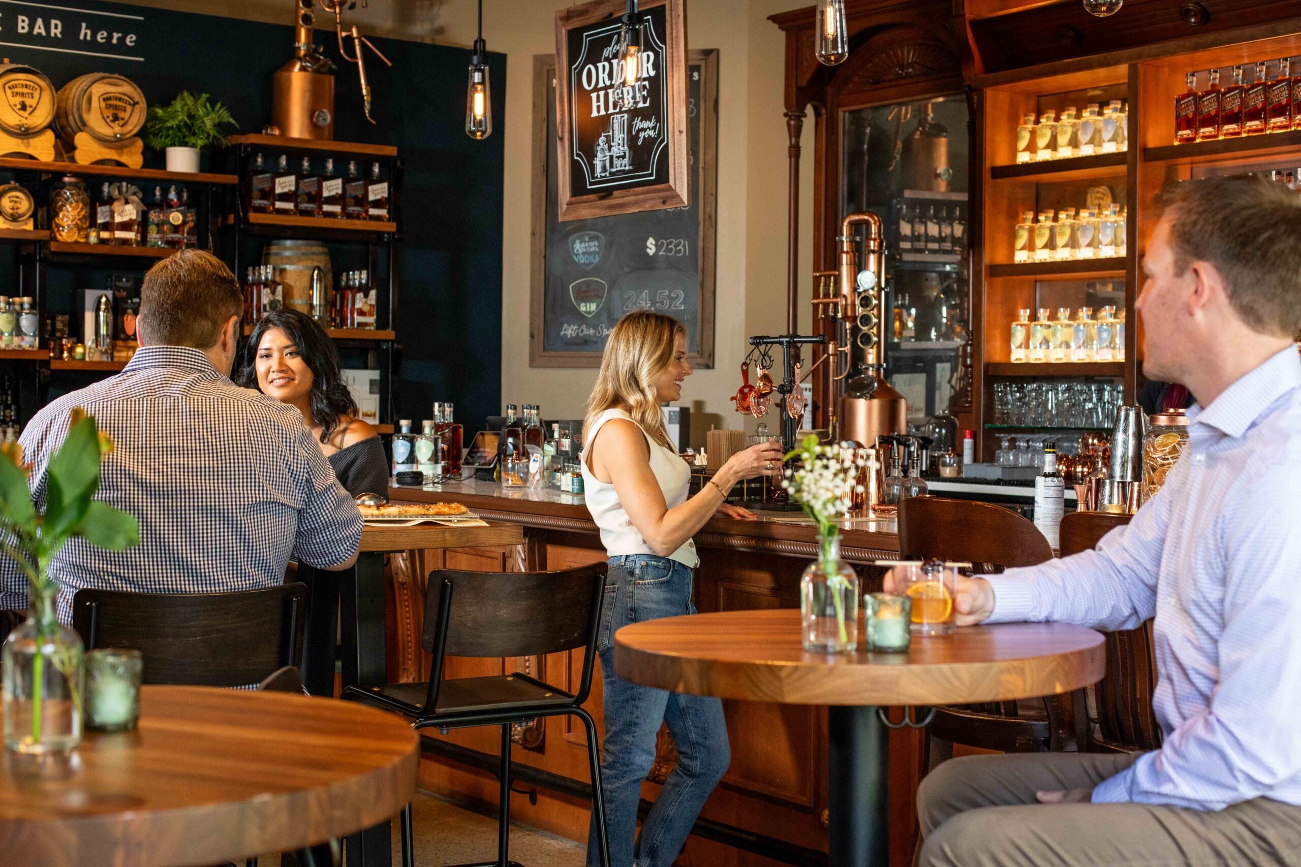People sitting at tables in a pub with shelves of drinks and decor.